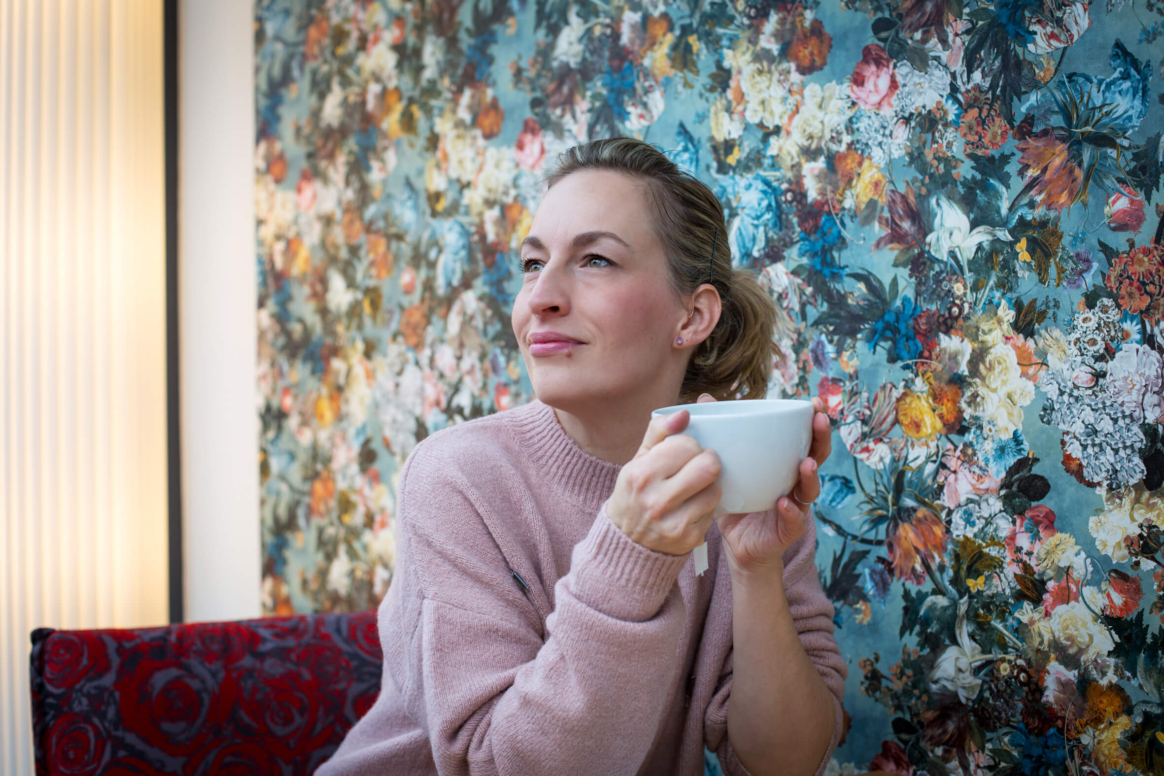 Frau sitzt mit einer Kaffeetasse in der Hand in einem Café und schaut nachdenklich zur Seite