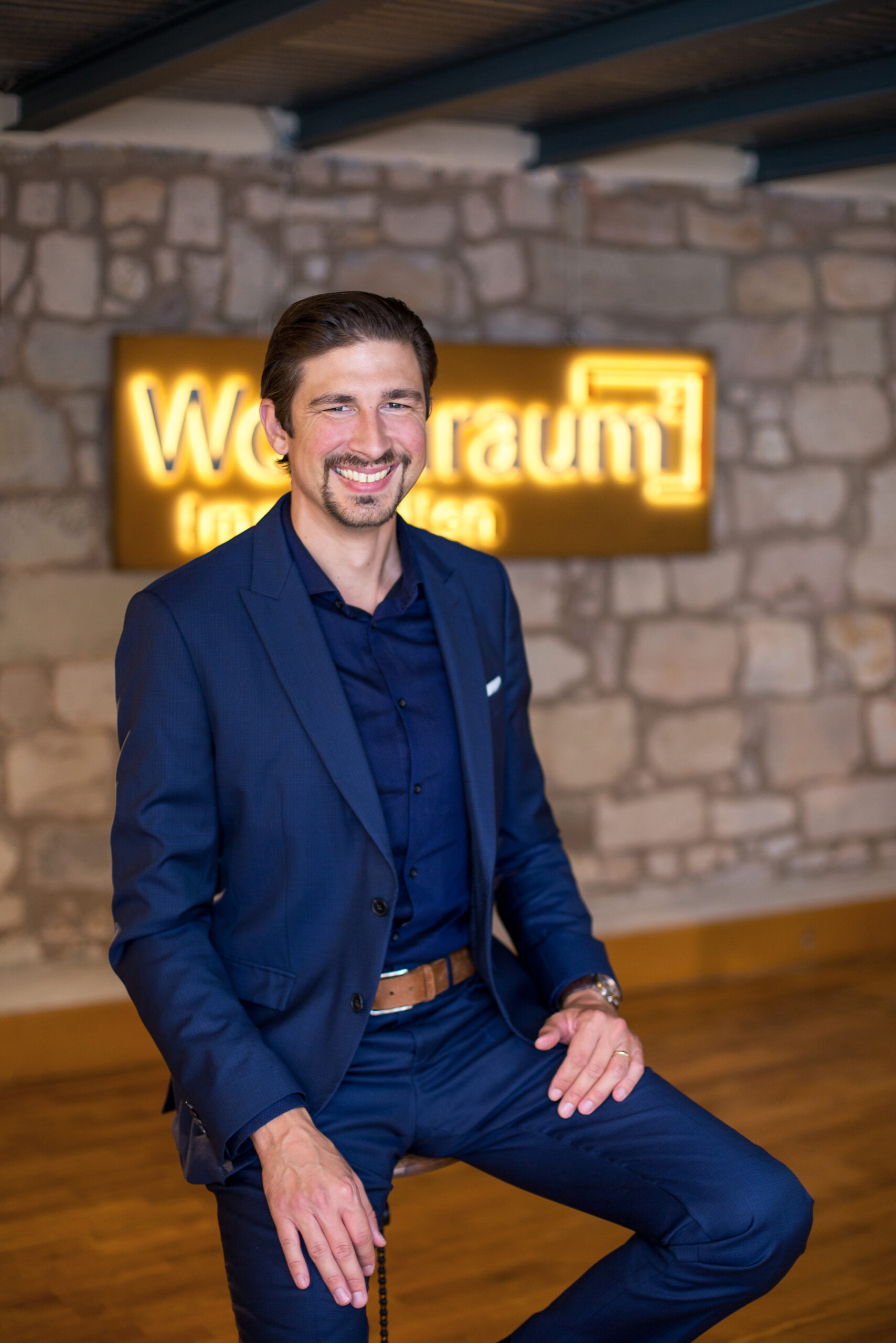 Portrait Mann indoor vor Steinwand mit beleuchtetem Firmenschild