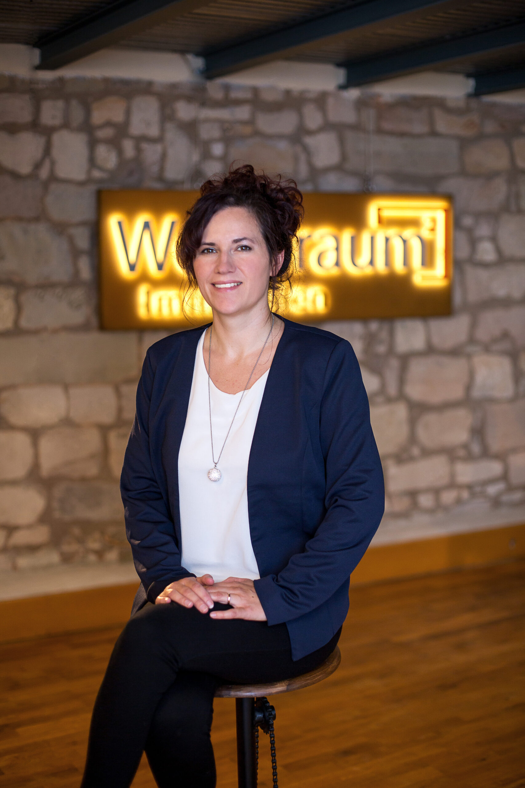 Portrait Frau indoor vor Steinwand mit beleuchtetem Firmenschild