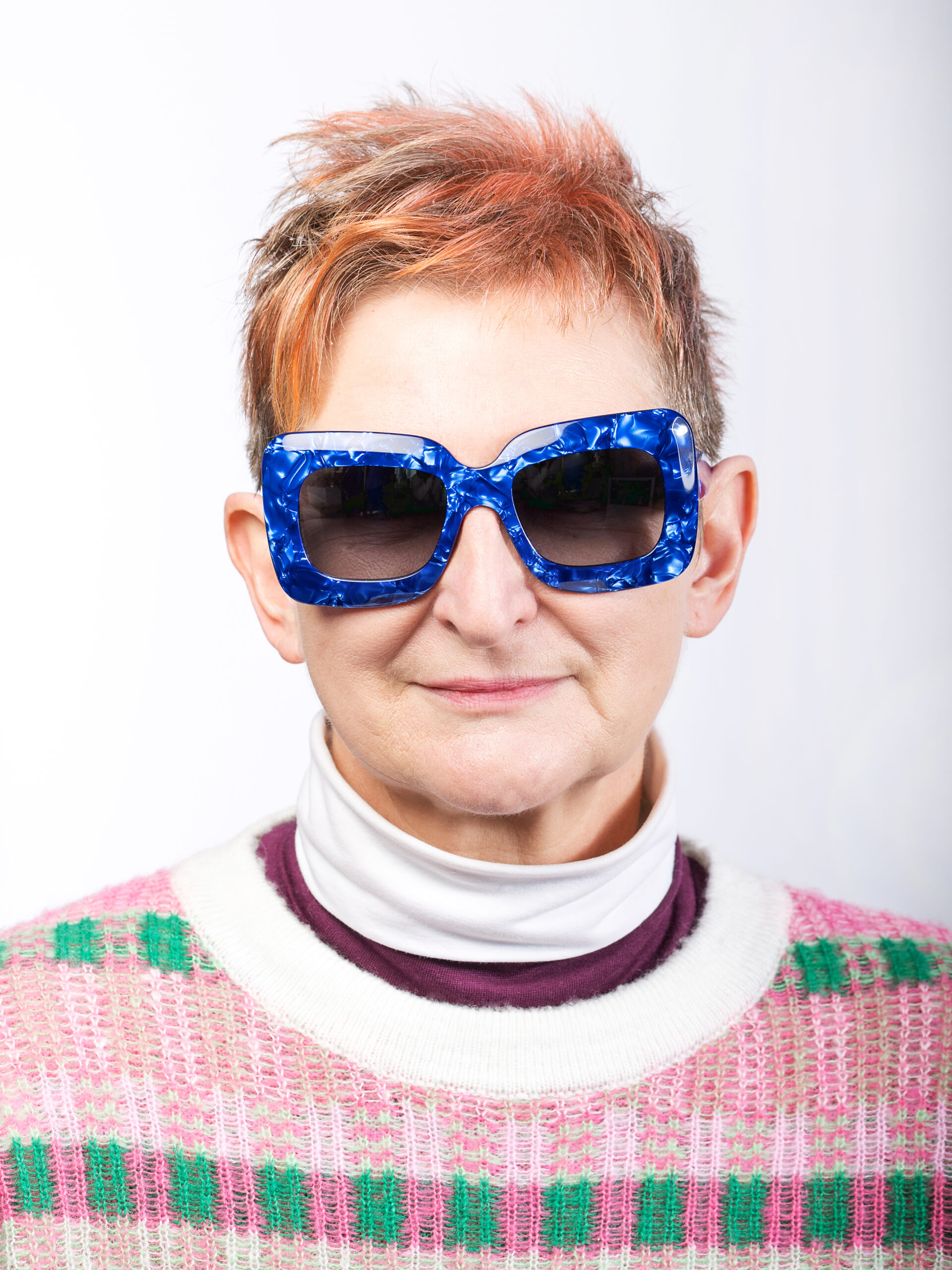 Studio-Portrait Frau mit pink-weiss-grünem Pullover und großer Sonnenbrille mit wuchtigem, blauen Rand
