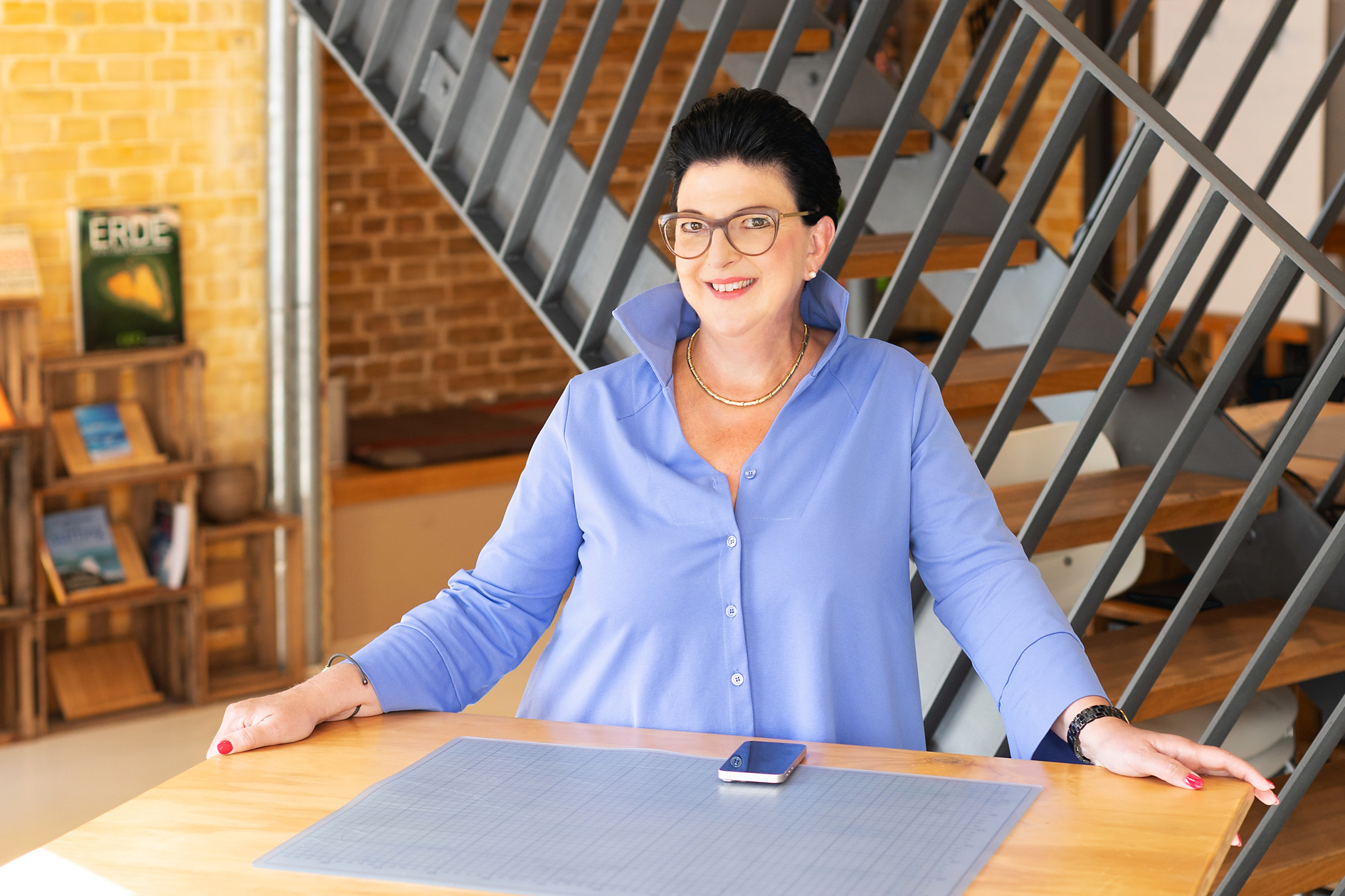 Frauen-Portrait indoor, Frau steht am Schreibtisch und schaut in die Kamera