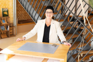 Frauen-Portrait indoor, Frau steht am Schreibtisch und schaut in die Kamera