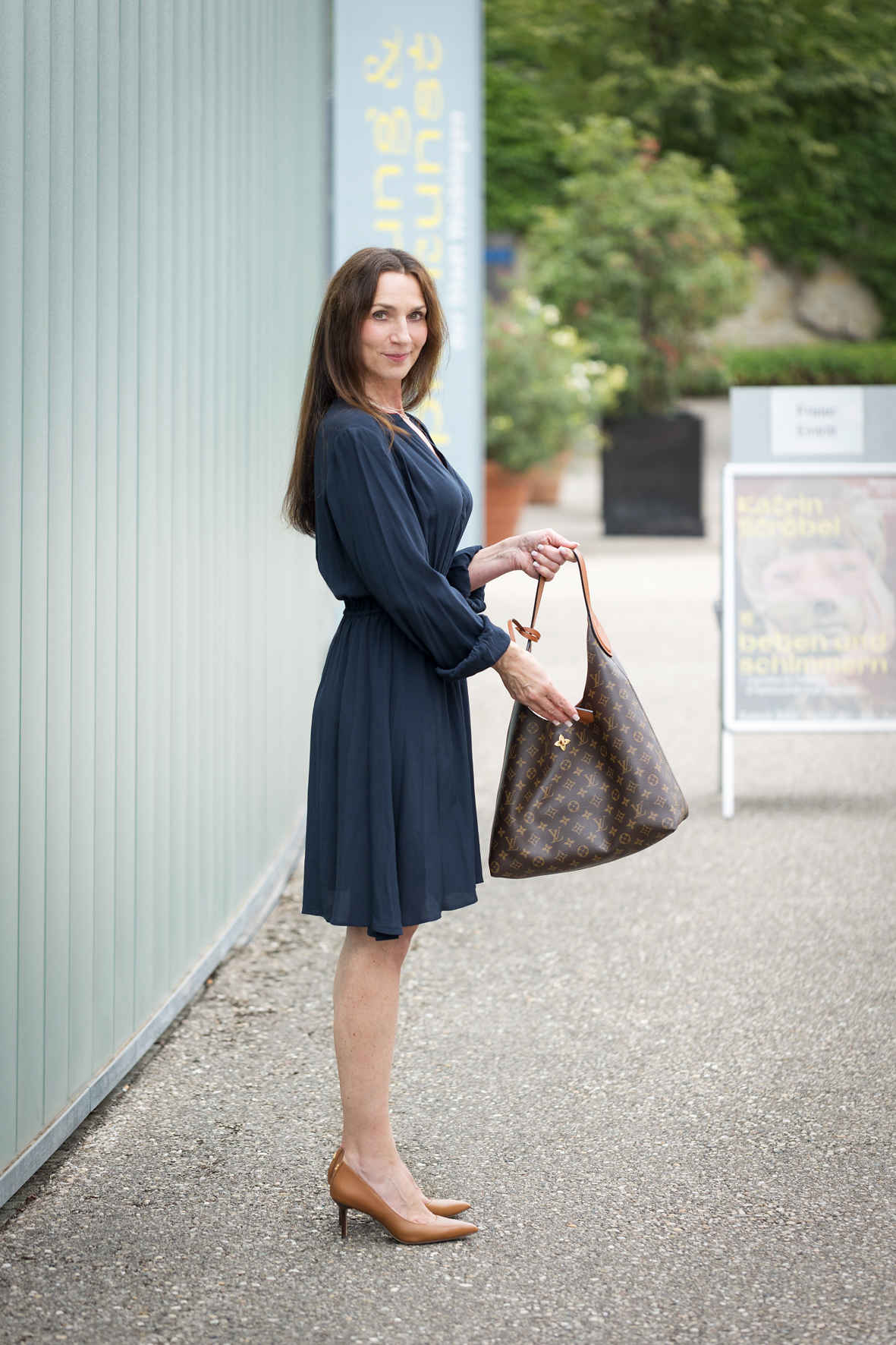 Bild einer Frau in einem dunkelblauen Kleid, hält eine Handtasche in der Hand